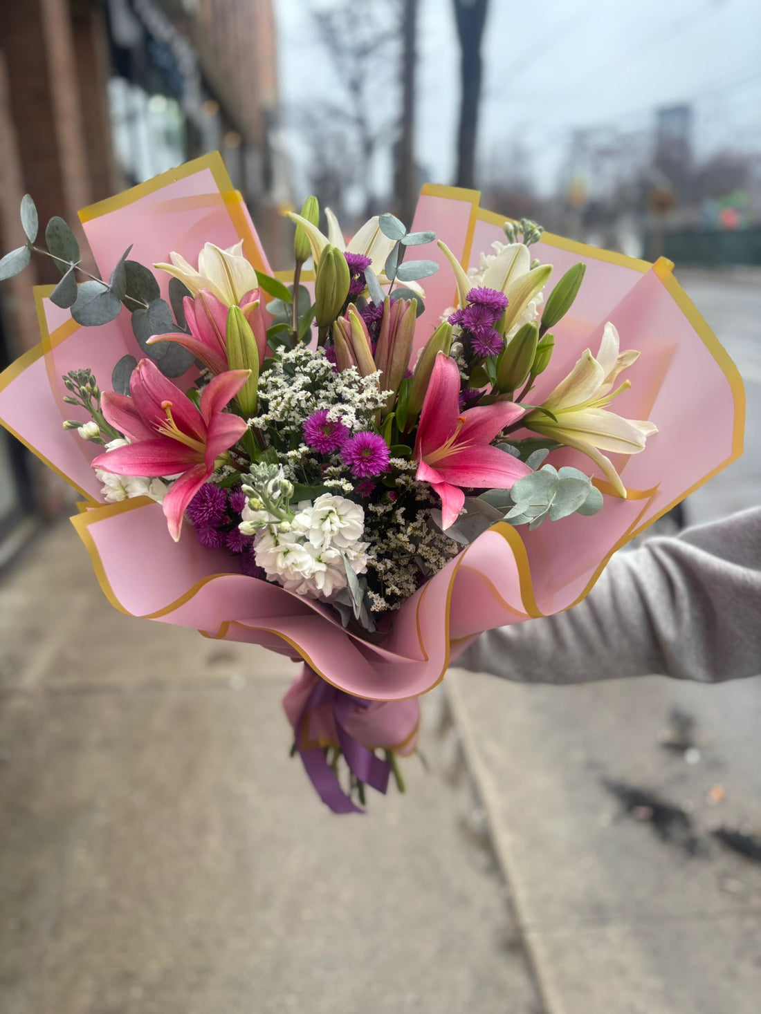 Bouquet of flowers wrapped in pink paper with a gold edge on a light background