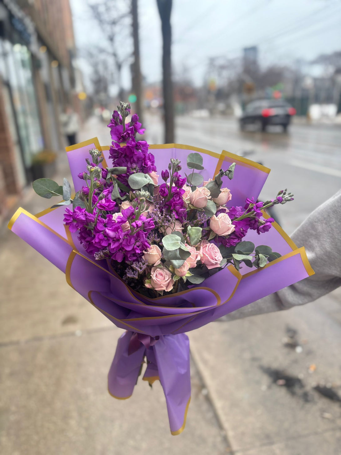 Bouquet of flowers wrapped in purple paper with gold accents on a light purple background