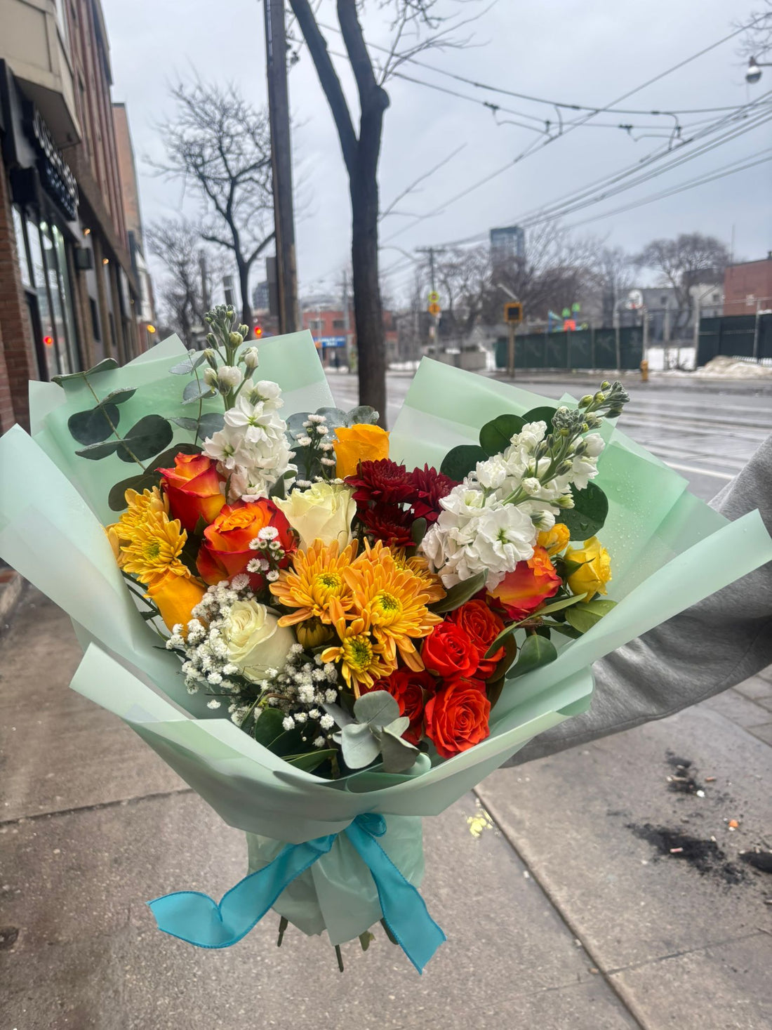 Bouquet of colorful flowers with a green wrap and blue ribbon on a light background