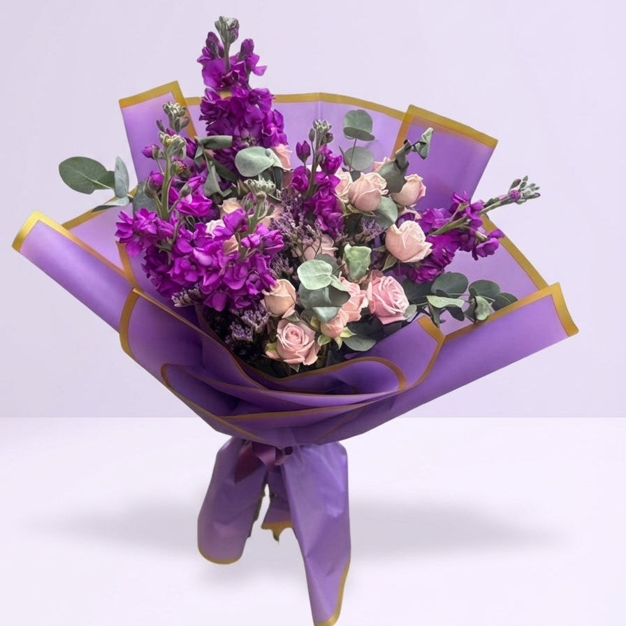 Bouquet of flowers wrapped in purple paper with gold accents on a light purple background