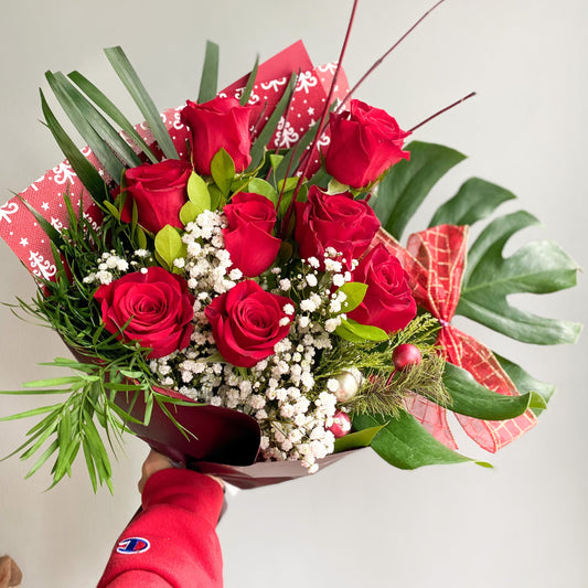 Christmas bouquet featuring 8 red roses surrounded by fresh Christmas greens, including pine and fir, creating a festive and elegant holiday arrangement 