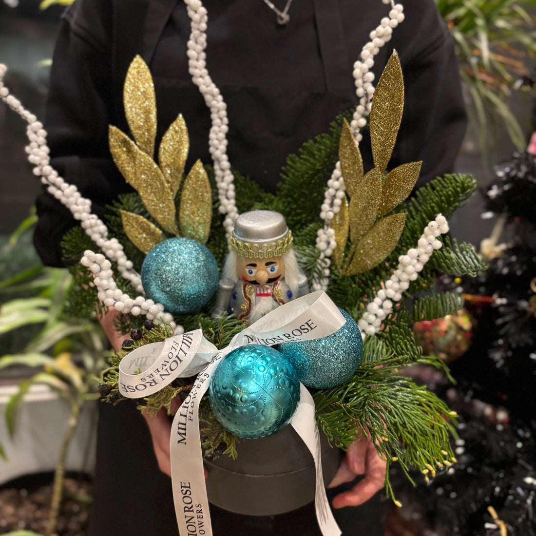 A festive Christmas flower box filled with red poinsettias, white chrysanthemums, and greenery, decorated with pinecones and red ribbon. The arrangement is placed in a wooden box with a rustic finish, evoking a cozy holiday atmosphere 