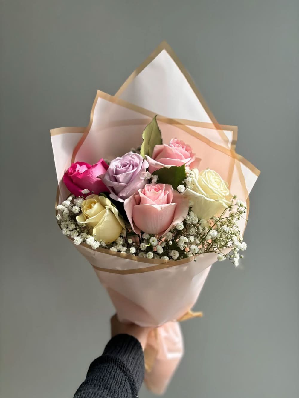 Bouquet of flowers wrapped in white paper with gold edges on a light background