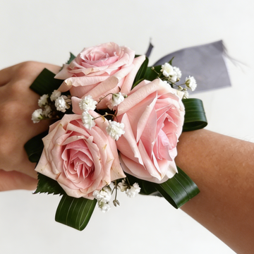 Wrist corsage with pink roses and greenery on a white background