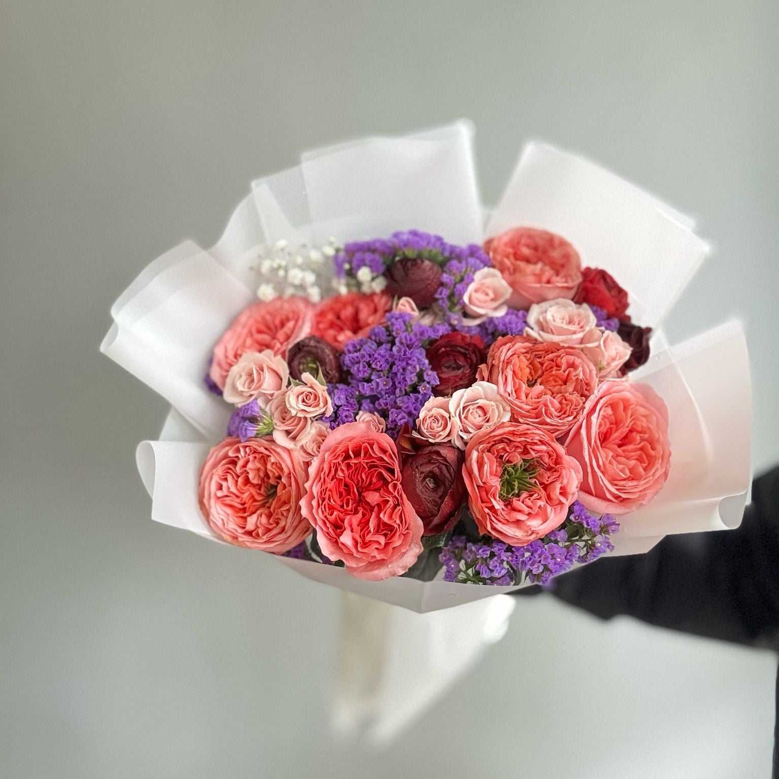 A vibrant and colorful mix of miniature English roses in various shades, including soft pink, peach, red, and white, showcasing their multi-layered, ruffled petals and delicate fragrance. These compact roses are displayed in a small garden or container, perfect for limited space or decorative purposes.