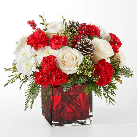 Festive red and white Christmas floral arrangement featuring red carnations, white roses, chrysanthemums, pinecones, hypericum berries, and fresh greenery, displayed in a red glass cube vase. Perfect for holiday decor or gifting."