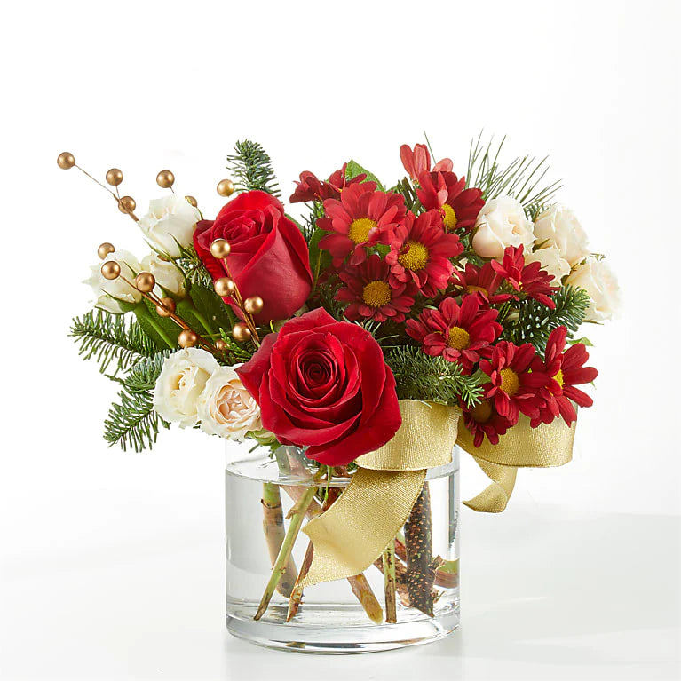 Festive sleigh Christmas floral arrangement featuring vibrant red roses, carnations, cream spray roses, hypericum berries, golden accents, and fresh greenery, arranged in a decorative white sleigh with gold snowflake details. Perfect for holiday decor or gifting