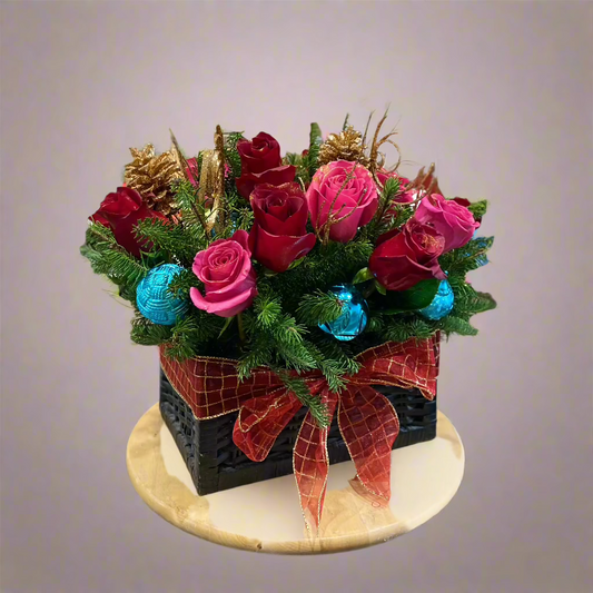 Christmas bouquet featuring red roses, white lilies, and festive greens like pine and fir, accented with berries and frosted pinecones in a decorative container