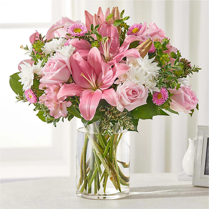 Sympathy flower arrangement with pink lilies, pink roses, daisies, and greenery in a clear glass vase for funerals or condolence gifts."

Let me know if you’d like variations for other uses (e.g., celebration of life, get well, or Mother's Day), or a longer version for accessibility-focused platforms.