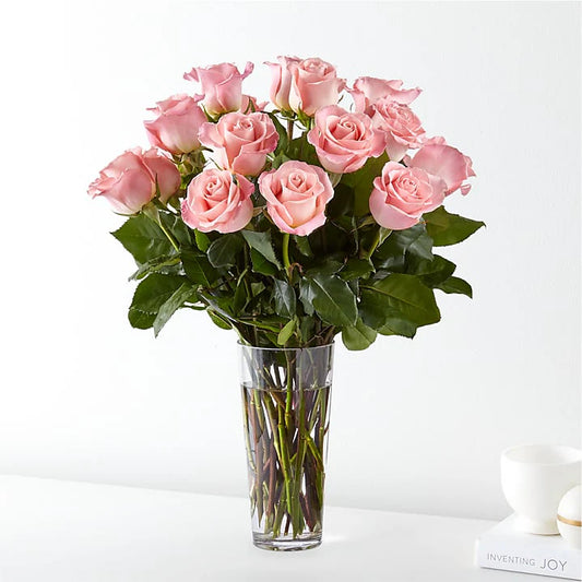 Arrangement of soft pink blush roses with greenery in a clear glass vase, ideal for romance, sympathy, or special occasions