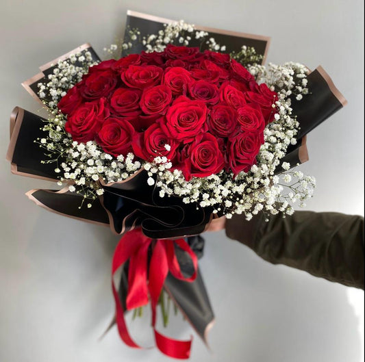 Bouquet of red roses with a red ribbon held by a person against a light gray background