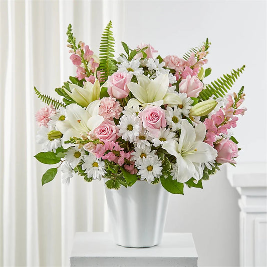 Bouquet of pink and white flowers in a white vase on a white surface with a white curtain background.