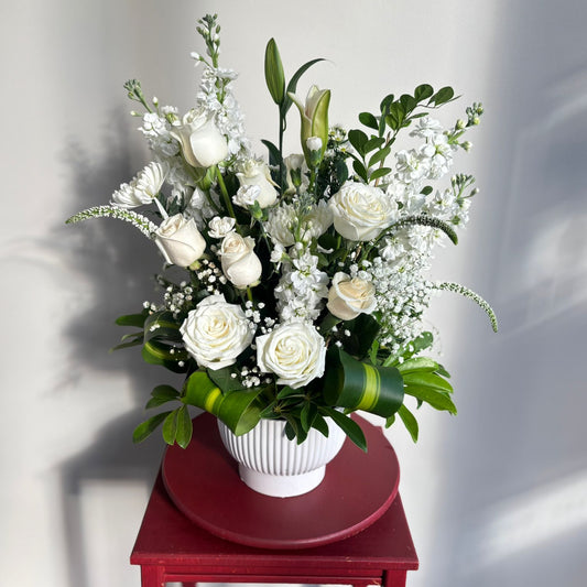 Bouquet of white flowers in a white vase on a red table against a light gray background