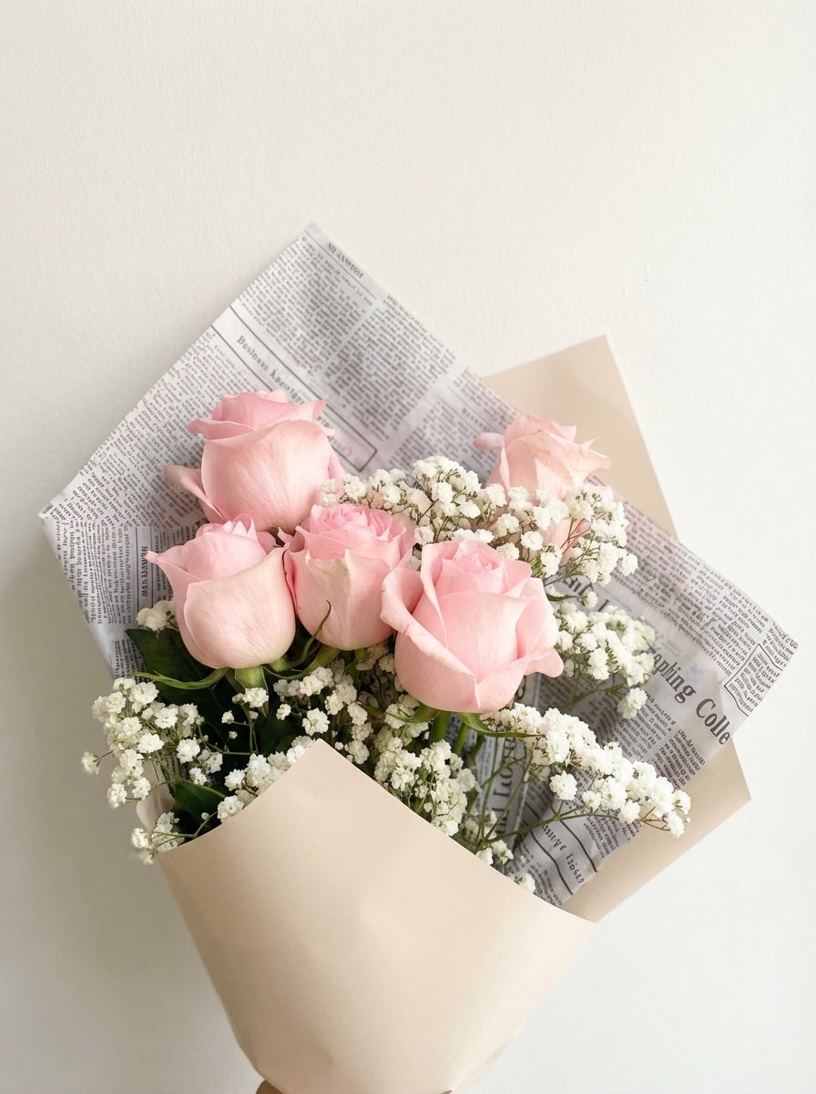 Bouquet of pink roses with baby's breath wrapped in newspaper on a light background