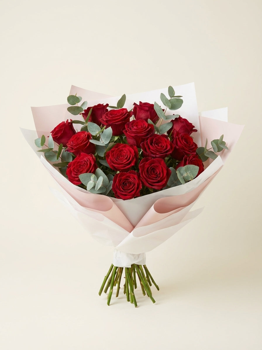 Bouquet of red roses wrapped in white paper on a light beige background