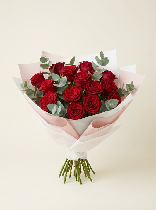 Bouquet of red roses wrapped in white paper on a light beige background