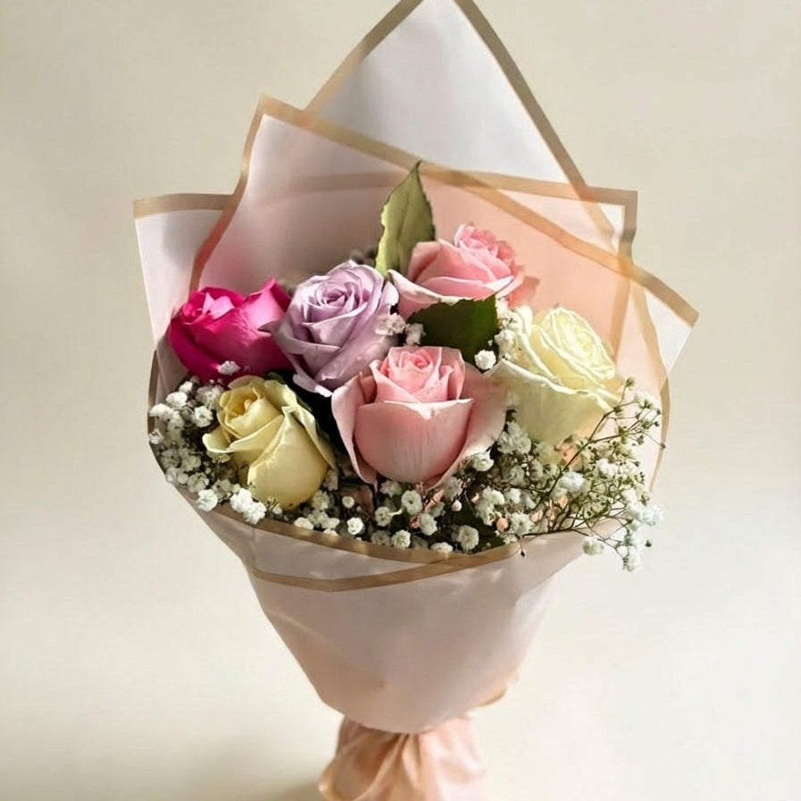 Bouquet of flowers wrapped in white paper with gold edges on a light background