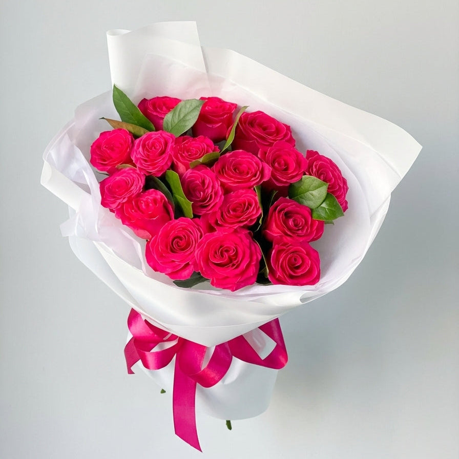 Bouquet of red roses wrapped in white paper with a pink ribbon on a light gray background