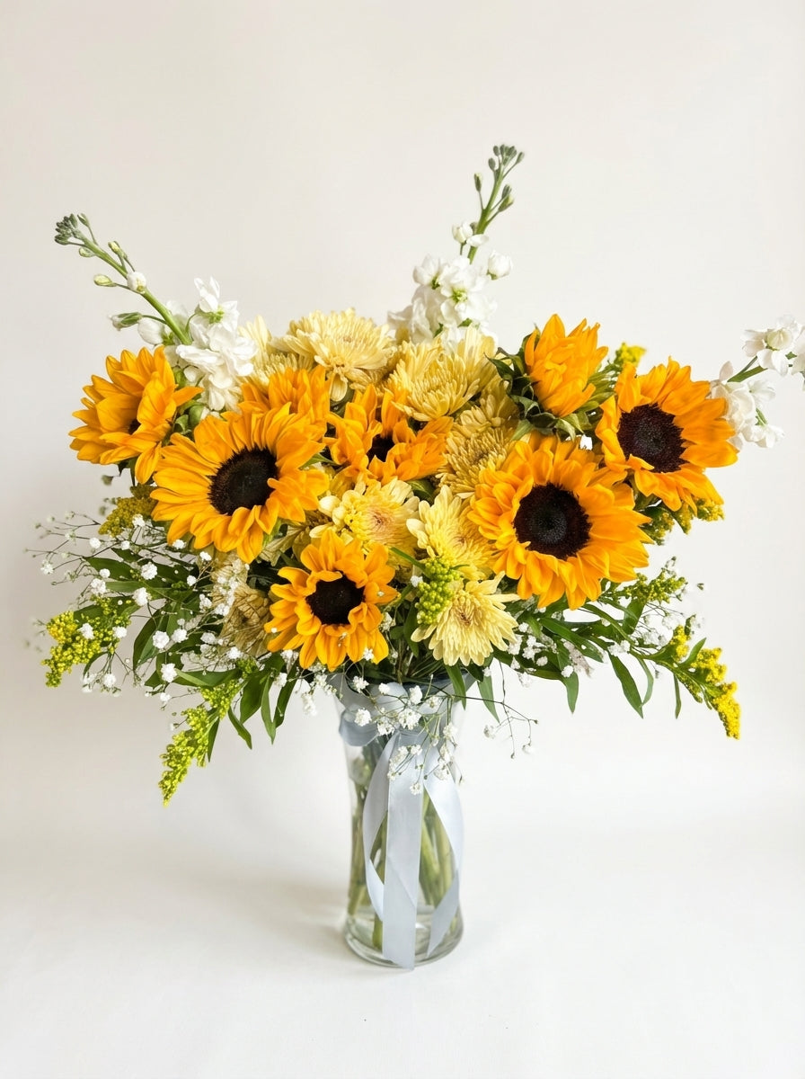 Bouquet of sunflowers and other flowers in a clear vase on a light background