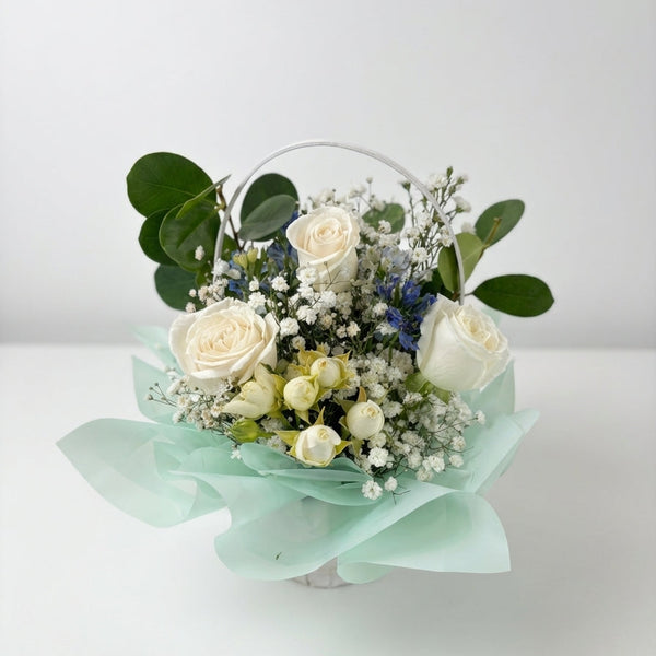 Bouquet of white roses and greenery in a transparent container on a light background