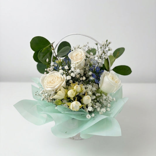 Bouquet of white roses and greenery in a transparent container on a light background