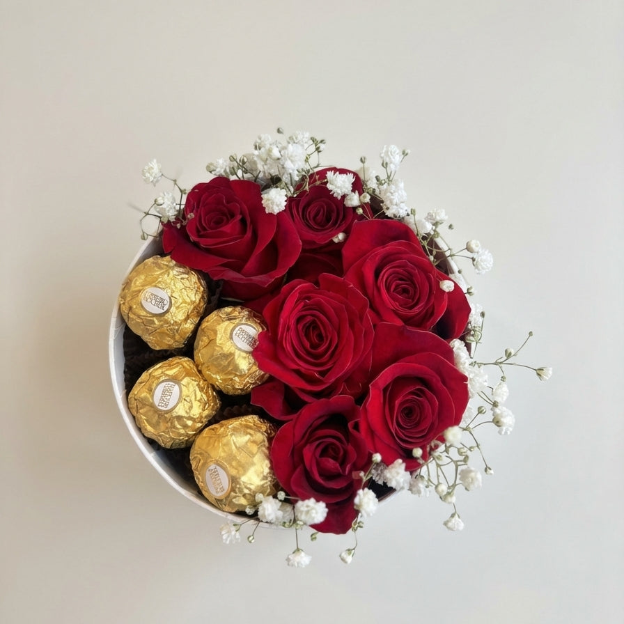 Round container with red roses and gold Ferrero Rocher chocolates on a light background