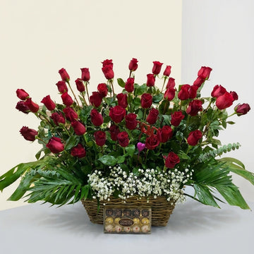 Bouquet of red roses in a basket with a box of chocolates on a light gray background