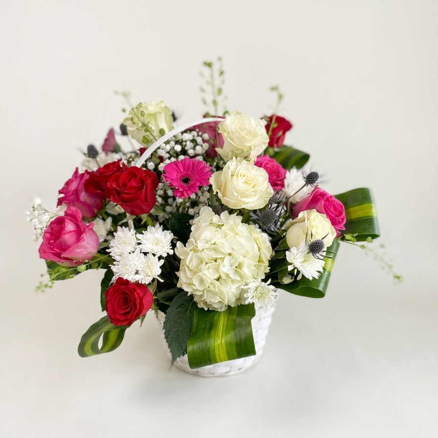 Bouquet of flowers with red, pink, white, and green colors in a clear vase on a light background