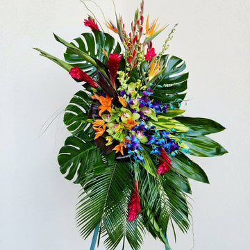 Colorful floral arrangement with tropical plants on a stand against a white background