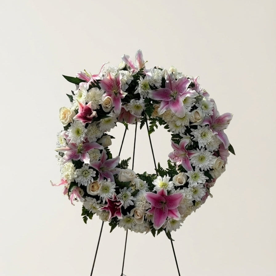 Floral wreath with pink and white flowers on a stand against a light gray background