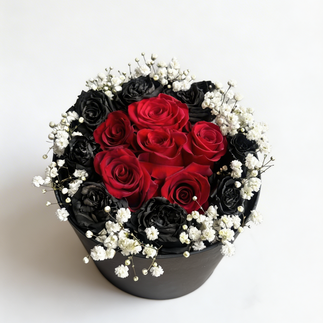 Round flower arrangement with red and black roses in a black container on a white background
