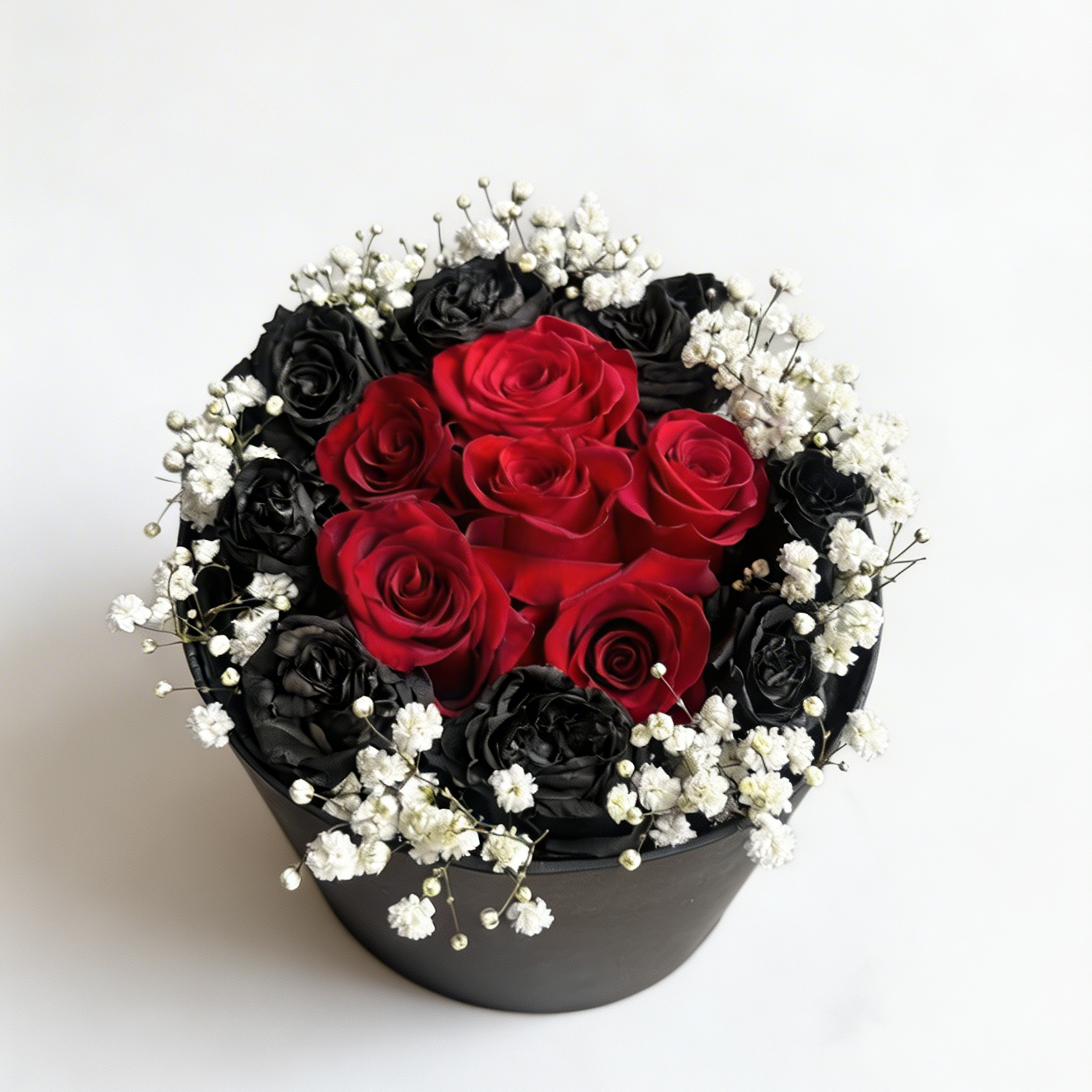 Round flower arrangement with red and black roses in a black container on a white background