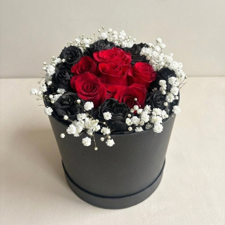 Round flower arrangement with red and black roses in a black container on a white background