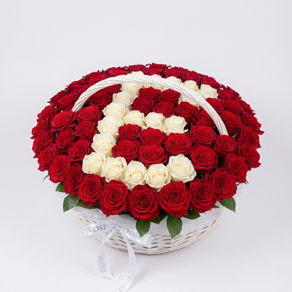 Heart-shaped arrangement of red and white roses in a basket on a light gray background