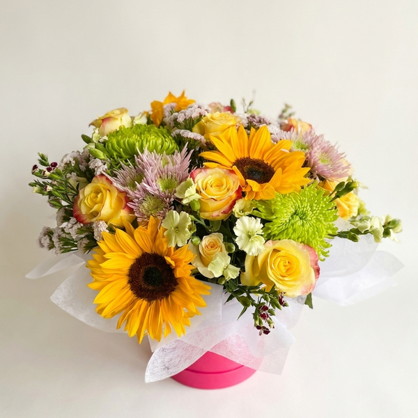 Bouquet of flowers with sunflowers and roses in a pink box on a light background