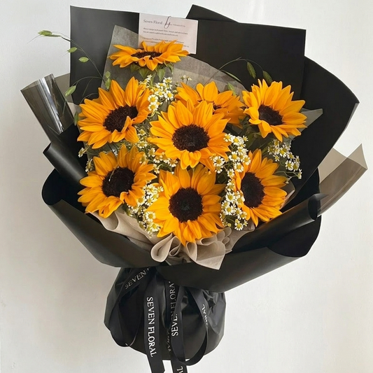 Bouquet of sunflowers wrapped in black paper with a Seven Floral ribbon on a white background