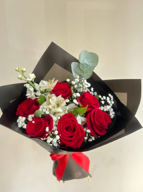 Bouquet of red roses and white flowers in black paper packaging on a light background