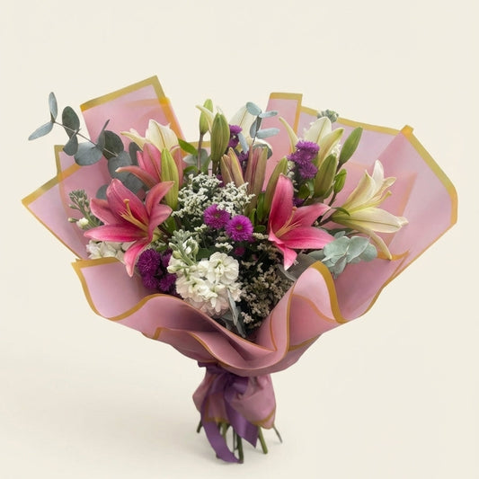 Bouquet of flowers wrapped in pink paper with a gold edge on a light background