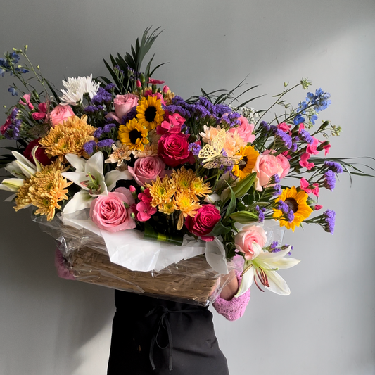 Vibrant mixed flower basket featuring a colorful assortment of roses, lilies, daisies, and greenery, elegantly arranged in a woven basket for a cheerful and bright gift