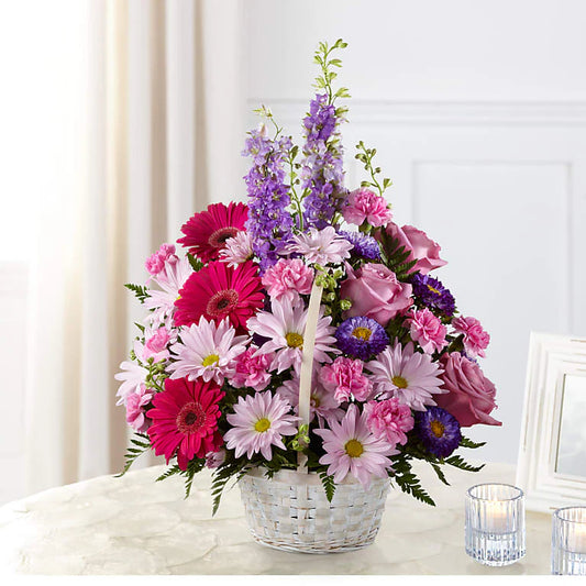Bouquet of colorful flowers in a white basket on a light surface with a white curtain background.