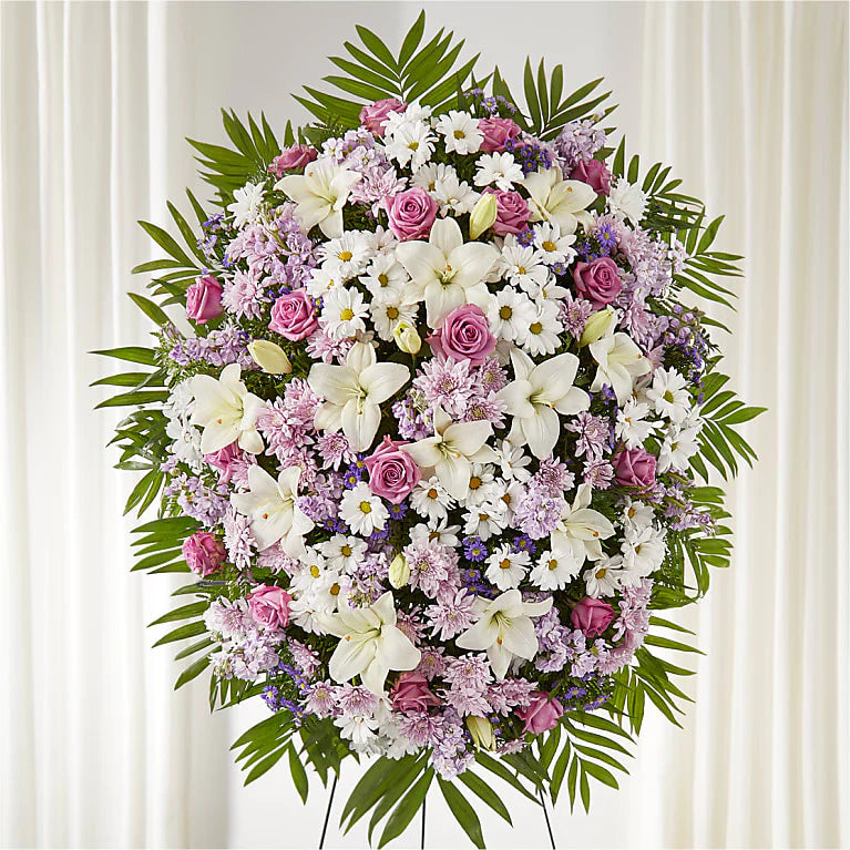 Purple and white flower spray with daisies, lilies, and roses arranged on an easel for funeral and memorial tributes.
