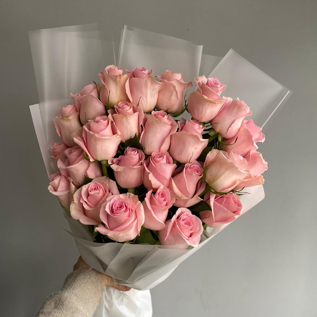 Bouquet of pink roses held by a hand against a gray background