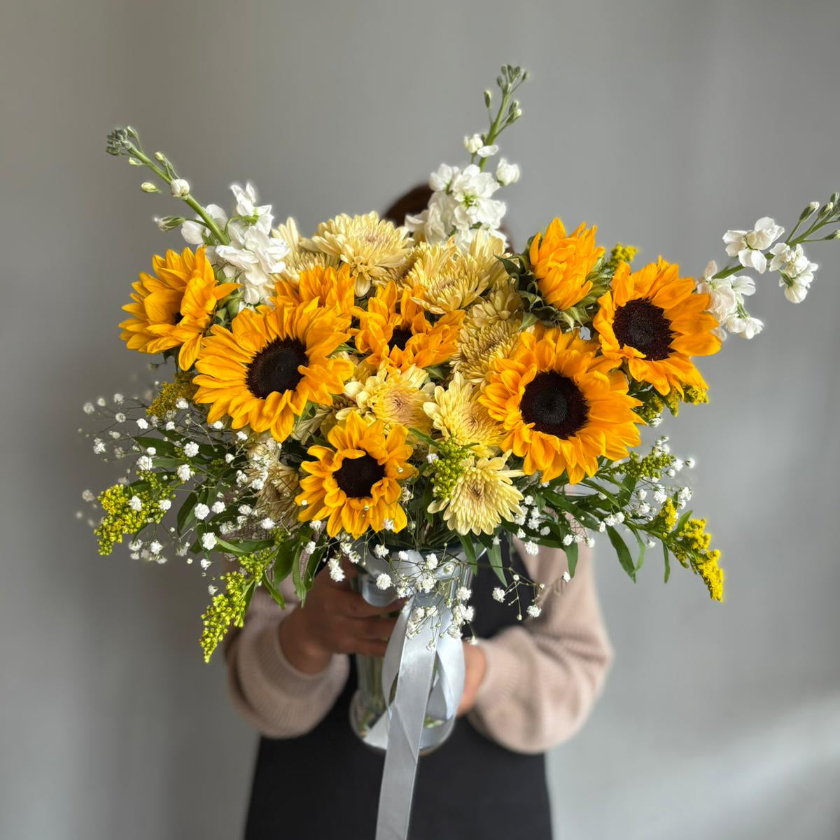 Bouquet of sunflowers and white flowers held by a person against a plain background
