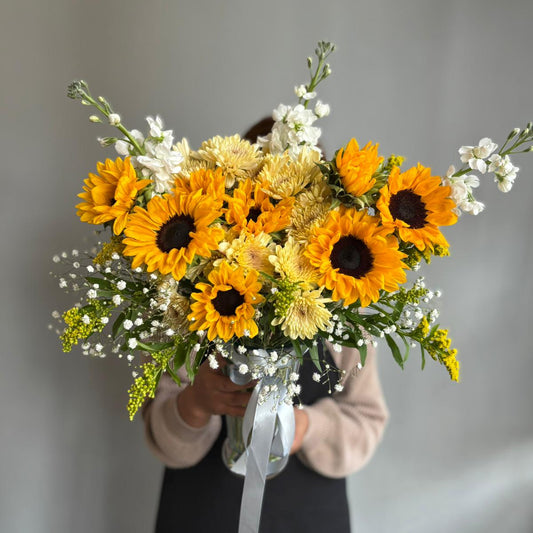Bouquet of sunflowers and white flowers held by a person against a plain background